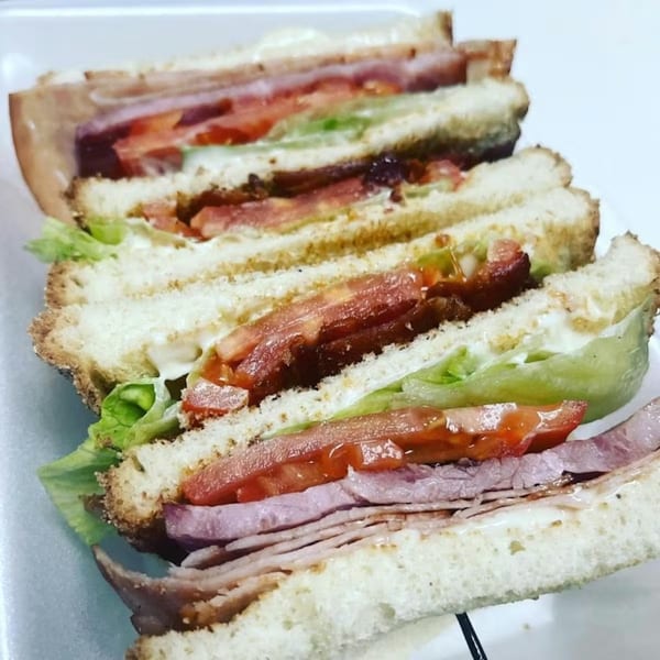 A stacked club sandwich with ham, bacon, lettuce, tomato, and mayonnaise on toasted bread.