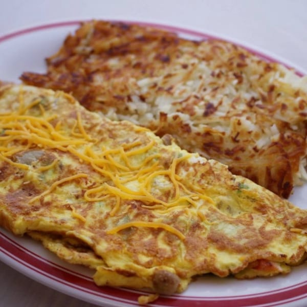 A cheese omelet with hash browns on a white plate with red stripes.