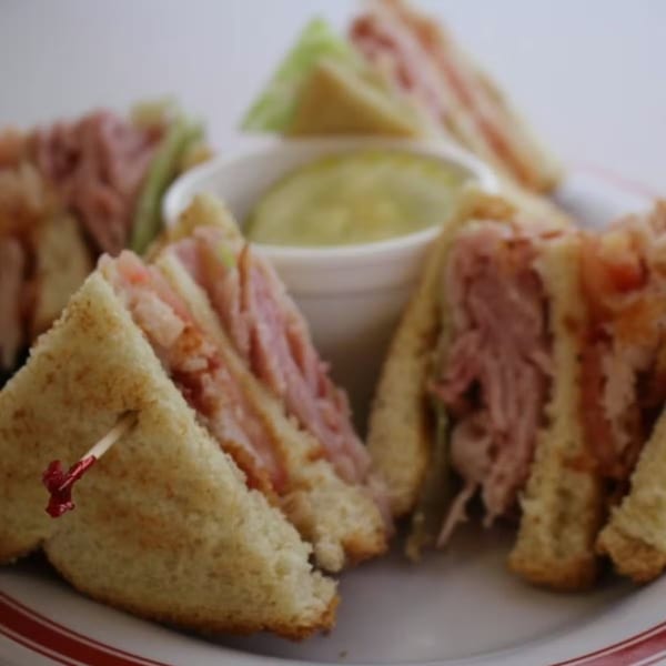 Club sandwiches with ham, lettuce, and tomato, served with a side of green dip.