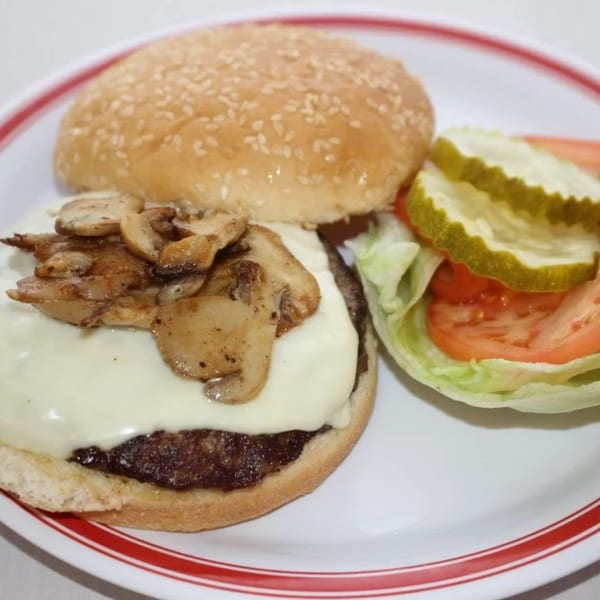 Mushroom Swiss burger with lettuce, tomato, and pickles on a white plate with red stripes.