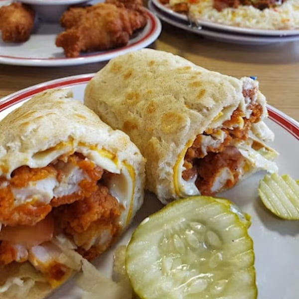 Two buffalo chicken wraps with melted cheese and lettuce, served with pickle slices on a plate.