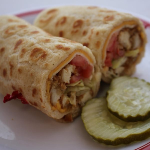 Two chicken wraps with lettuce, tomato, and cheese, served with pickle slices.